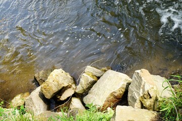 Flussufer Panorama mit Felsbrocken am Flussufer und Wellen im Wasser bei Sonne im Frühling 