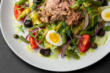 French salad Nicoise with tuna, egg, green beans, tomatoes, olives, lettuce, onions and anchovies on a gray background. Healthy food