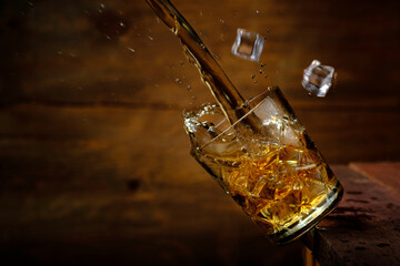 A splash of whiskey in a falling glass with ice from a wooden table. Rustic style.