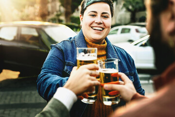 Happy young people at happy hour toasting beer glasses and having fun bonding - group of best...