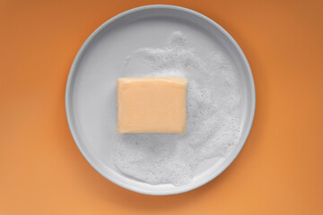 Top down view mockup peach pastel orange color vitamin c soap bar square shape with foam bubbles water on white plate and solid plain orange as background