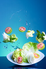 Obraz na płótnie Canvas fresh vegan flying salad with water splash on blue background in vertical shot with bright light