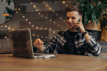 Positive young businessman making phone call on smartphone and talking about startup project while...