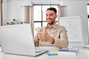 Fototapeta premium distance education, school and remote job concept - happy smiling male teacher with laptop computer having online class at home office showing thumbs up