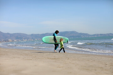 father teaching his child surfing on the beach by the sea. excited girl or boy doing execises developing new skills. Surfing, fatherhood concept