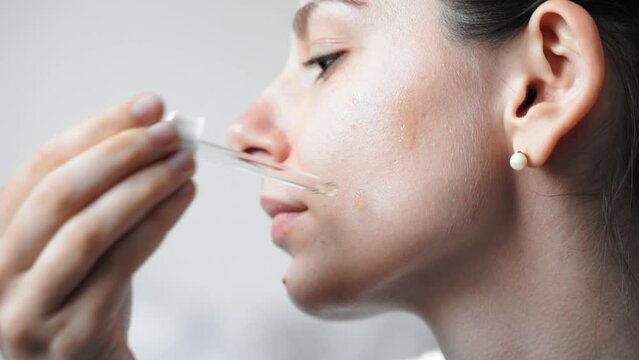 Close up of female young caucasian woman applying serum or drop oil skin care product on her face. Wellness and spa at home