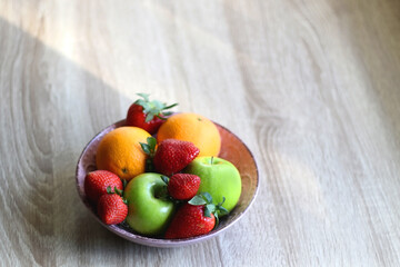 Pink bowl filled with fresh apples, oranges and strawberries on wooden table. Selective focus.