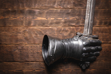 Old knight sword in the armor glove on the wooden flat lay table background with copy space.