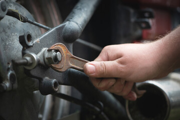 Biker unscrews a motorcycle wheel with a wrench close-up.