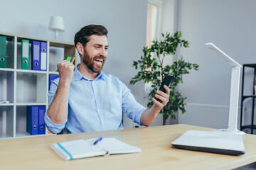 Happy businessman reading good news from the phone, man working in the office