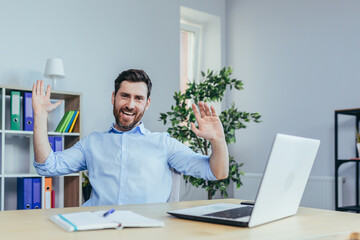 Businessman working in a bright office, celebrating the success of dancing at the table with a laptop