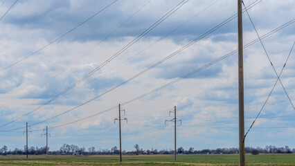 High voltage post on blue sky with clouds background. Electrical net of poles on blue sky and spring meadow.