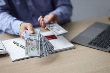 Wealthy businessman counting money and holding cash on his desk is offering you his paycheck. The...