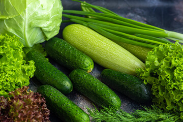Fresh vegetables for salad. Tomatoes and lettuce, cucumbers with zucchini and cabbage with dill. Spring harvest, benefits and vitamins. On a dark background.