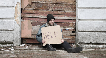 Homeless man sits and holds piece of cardboard with inscription Help. Refugee looking for job. Male...