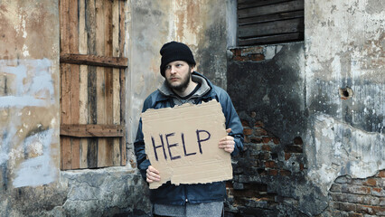 Homeless holds piece of cardboard with inscription Help. Refugee at abandoned building looking for...