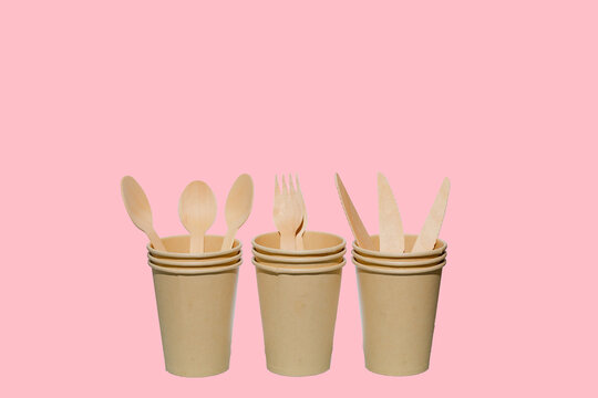 A set of brown eco paper cups for coffee, tea, drink. Wooden fork,knift and spoon  isolated on pink background. Environmental friendly concept.