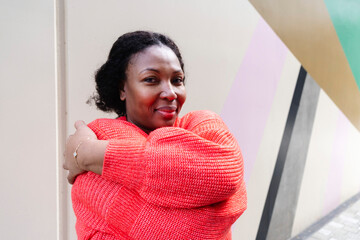 Smiling woman wearing orange sweater hugging self