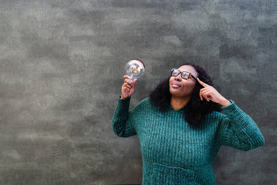 Thoughtful woman holding light bulb in front of gray wall