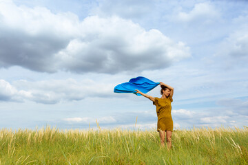 Woman holding aloft wind-swept blue scarf at meadow