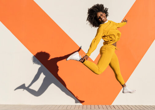 Happy woman jumping by wall on sunny day