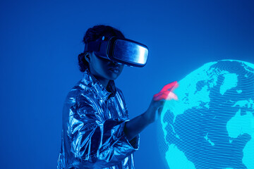 Woman wearing virtual reality simulator touching earth on screen against blue background