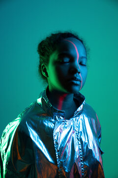 Laser light falling on woman's face standing with eyes closed against green background