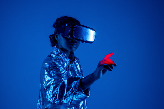 Young woman wearing virtual reality simulator gesturing by standing against blue background