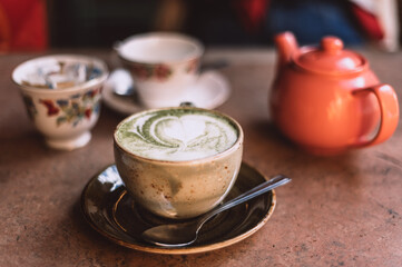 Green Matcha Latte, popular trendy tea with latte art heart shape on top. Served in cafe in ceramic mug on rustic table. Strong shadows and summer sun light