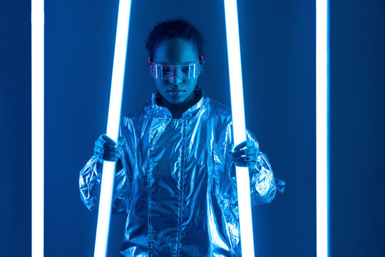 Woman in smart glasses holding illuminated neon light against blue background