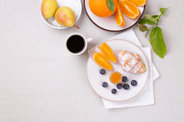 Breakfast with a cup of coffee, fresh croissant , jam and ripe blueberries and juicy oranges, pears on a white background, flat lay, copy space