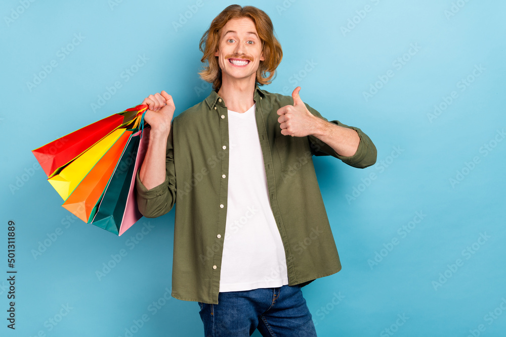 Poster portrait of attractive funky cheerful guy holding bags showing thumbup advert isolated over pastel b