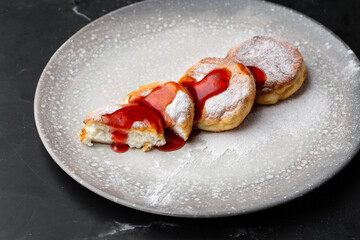 Cottage cheese pancakes, Syrniki or Cheesecakes with red sauce isolated on black marble background. Homemade food. Tasty breakfast. Selective focus.