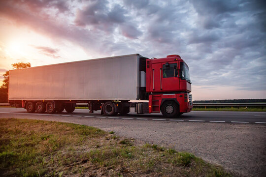 A modern truck with a semitrailer refrigerator transports cargo against the backdrop of an evening sunset in summer. Road freight industry. Goods turnover, sanctions