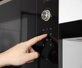 A man's hand presses the touch panel of a modern microwave oven to select the power and function of heating food. Close-up