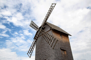 Beautiful old wooden mill in the village against the background of blue sky and clouds. Traditional, historical
