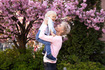 Mom and little son in nature playing at spring park. Little boy and mother have a good time on weekend activity in the blooming Sakura gardens