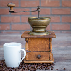 Manual coffee grinder, cup of coffee with scattered coffee beans on a wooden surface. Square format