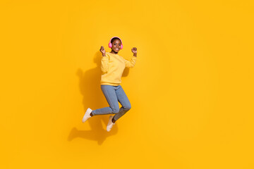 Fototapeta na wymiar Full length body size view of attractive cheerful girl fan jumping listening hit pop isolated over bright yellow color background