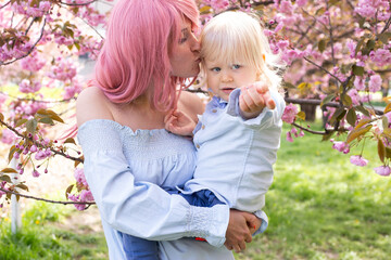 happy mother and little son are having fun in the blooming Sakura gardens. Portrait woman hugging little baby boy