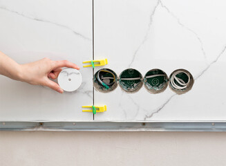 Drilled holes for sockets in the master's hand against the background of porcelain tiles. Repair in...