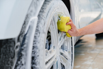 self-service car wash. a man in a work jumpsuit washes the wheels with a sponge 