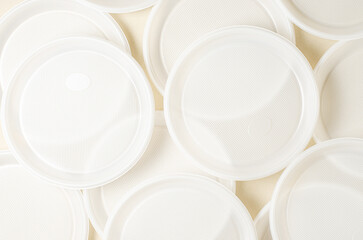 Disposable white plastic tableware on a beige background. The concept of nature pollution