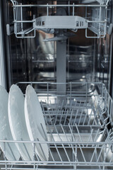 Well-washed dishes in the dishwasher. Built-in dishwasher with white plates in front. dishwasher concept