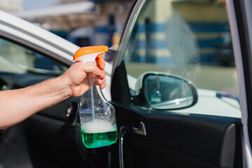 self-service car wash. a man washes the car window with glass cleaning liquid