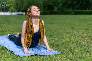 Woman yogi with dreadlocks stretching doing practicing Upward Facing Dog Pose Urdhva Mukha Svanasana pose on yoga mat. Relaxing in the morning. Fitness instructor coach showing exercises 
