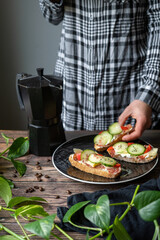 person reaching for coffee maker and a colourful sandwich from black plate and wooden table