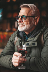 Senior man enjoying a glass of red wine at the bar. A client in a dark pub.