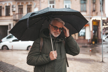 Senior man suffering from migraine in rainy weather. A man under an umbrella in cold weather.