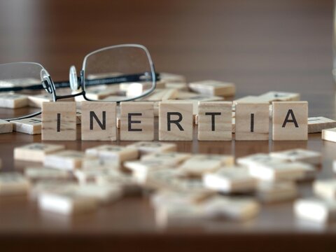 inertia word or concept represented by wooden letter tiles on a wooden table with glasses and a book
